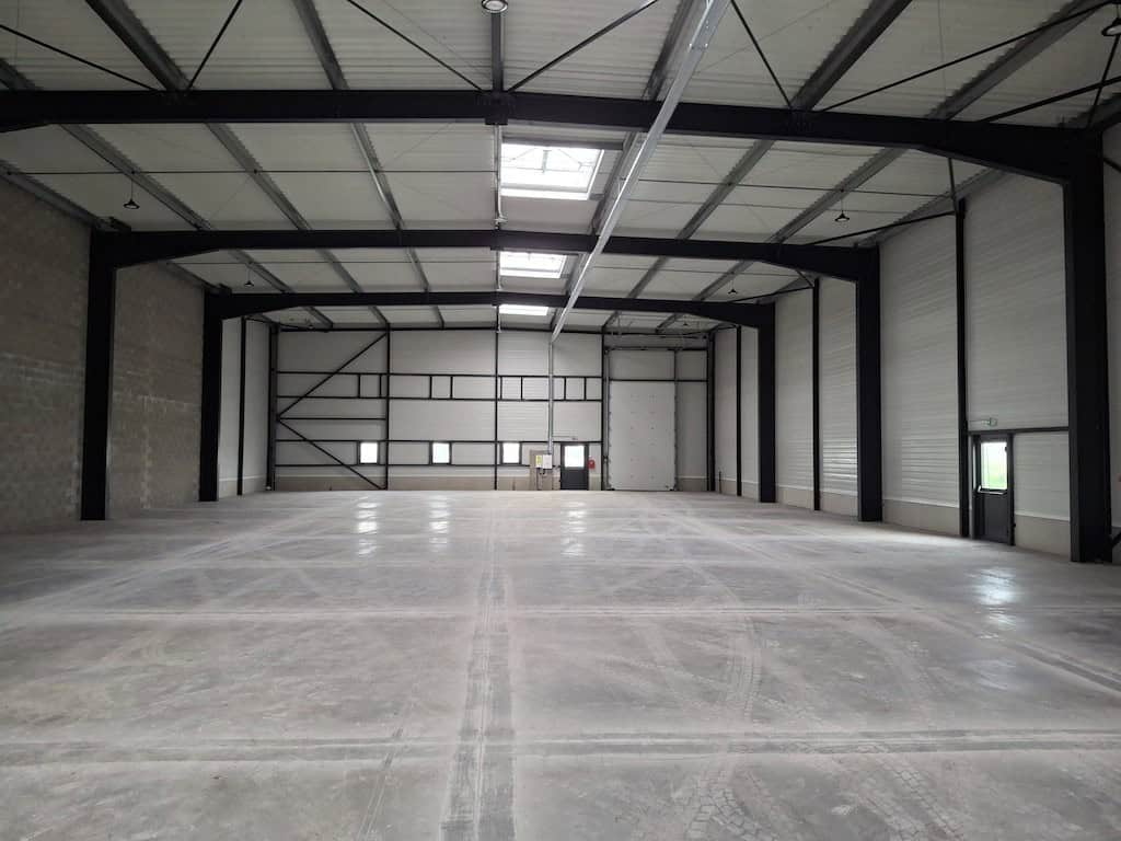 Grand entrepôt vide avec plafond haut et structure métallique.